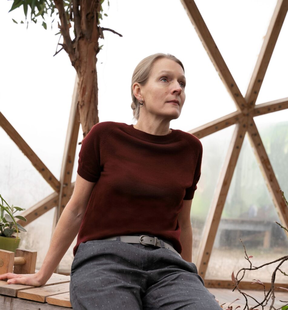 Hanne Linding in a greenhouse with a red sweater and gray pants.