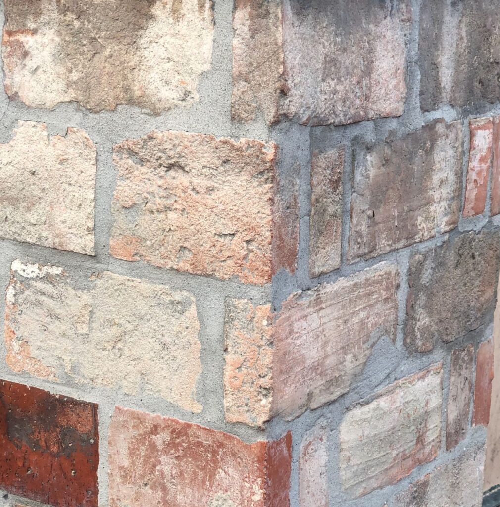 Brick corner with different colored bricks and grey mortar. Front Hanne Linding.